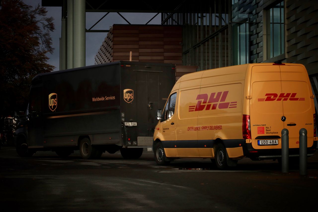 about-img DHL and UPS delivery trucks parked at night near a modern building, ready for logistics operations.